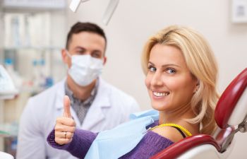 satisfied female dental patient in dental chair showing thumb up
