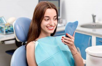 satisfied woman after dental treatment looking at her teeth in mirror
