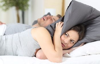 snoring man and annoyed woman covering ears with pillow