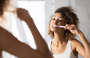 Afro-American woman brushing teeth in front of the bathroom mirror.